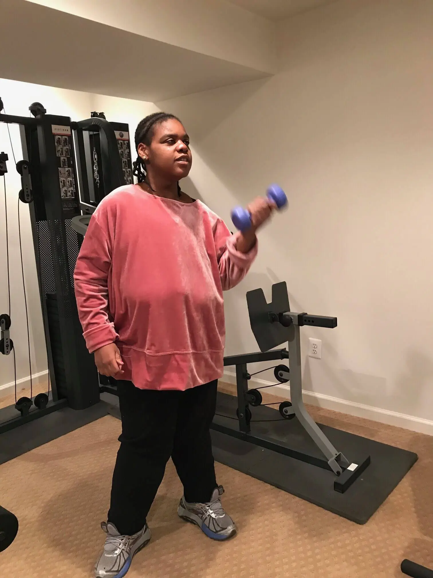 Person lifting a purple dumbbell in a home gym setting.