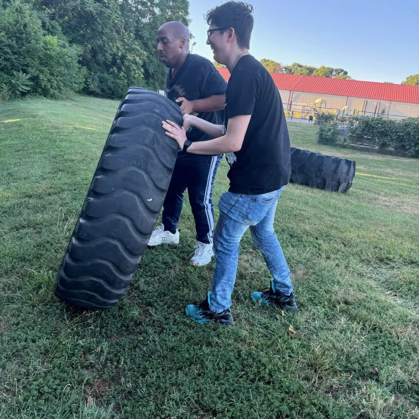 Two people flipping large tractor tire outdoors